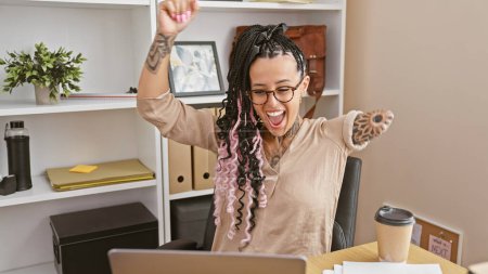 Photo for Joyful hispanic woman worker, an amputee, celebrating business win at office, laughing while working on laptop! - Royalty Free Image