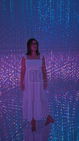 Photo for Radiant hispanic woman, beautiful in glasses, immerses in a futuristic light exhibit at the cutting-edge museum, awash in a fluorescent neon display of modern technology and creativity. - Royalty Free Image