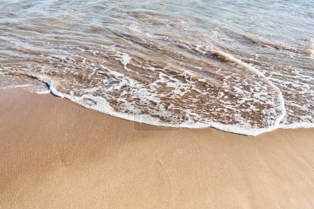 Foto de Las suaves olas bañan la arena dorada en un entorno de playa tranquilo y soleado sin personas presentes. - Imagen libre de derechos
