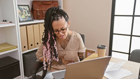 Téléchargez les photos : Femme hispanique en détresse, un travailleur d'affaires amputé, aux prises avec des maux d'estomac au bureau tout en travaillant sur ordinateur portable - en image libre de droit