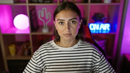 Téléchargez les photos : Une jeune femme hispanique pose dans une salle de jeux avec éclairage ambiant, projetant confiance et style contemporain. - en image libre de droit