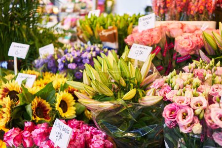 Une gamme vibrante de fleurs assorties à vendre, présentant tournesols, lis, roses et delphiniums, avec des étiquettes de prix visibles dans le marché d'un fleuriste.