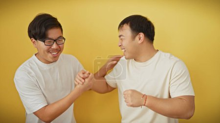Photo for Two asian men in white shirts smiling and shaking hands against a yellow background, radiating a sense of friendship and companionship. - Royalty Free Image