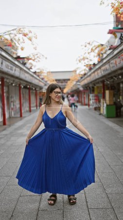 Photo for Beautiful hispanic woman spinning around in dress on nakamise street, glasses sparkling in the japanese sun, a cheerful dance amidst urban travel - Royalty Free Image