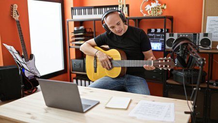 Foto de Joven músico hispano que tiene clase de guitarra clásica en línea en el estudio de música - Imagen libre de derechos