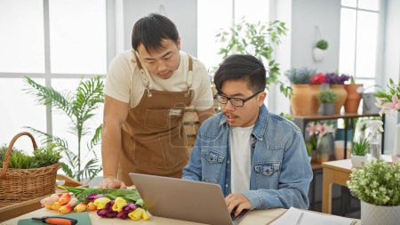 Two male coworkers collaborate in a flower shop using a laptop surrounded by colorful floral arrangements and plants.