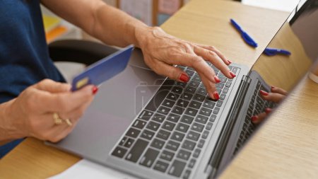 Foto de Una mujer mayor de compras en línea con una tarjeta de crédito en un entorno de oficina en casa. - Imagen libre de derechos