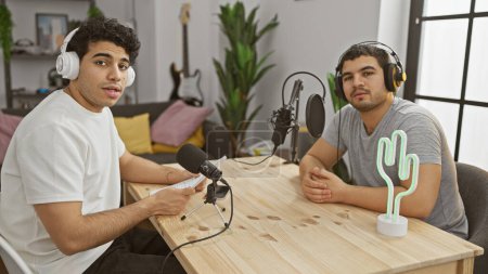 Photo for Two men podcasting indoors with microphone, headphones, table, cactus light, and guitar. - Royalty Free Image