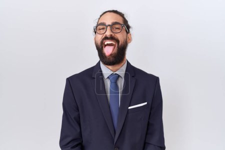 Téléchargez les photos : Homme hispanique avec barbe portant costume et cravate langue collante heureux avec une expression drôle. concept d'émotion. - en image libre de droit