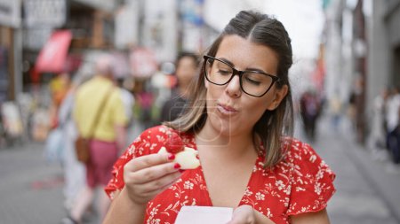 Photo for Gorgeous hispanic girl in specs relishing strawberry japanese mochi on osaka's famous dotonbori street - Royalty Free Image