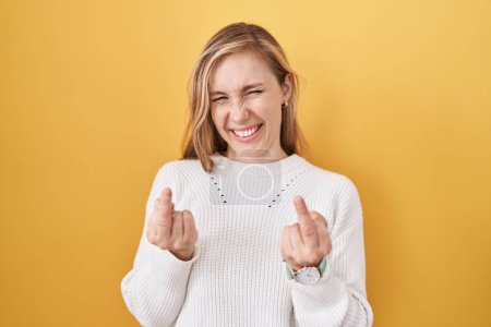 Foto de Young caucasian woman wearing white sweater over yellow background showing middle finger doing fuck you bad expression, provocation and rude attitude. screaming excited - Imagen libre de derechos
