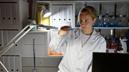 Photo for A focused young woman scientist examines a blue solution in a flask in a well-equipped laboratory. - Royalty Free Image