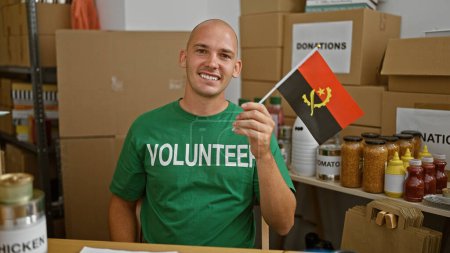 Jeune homme hispanique volontaire souriant confiant tenant drapeau d'angola au centre de charité