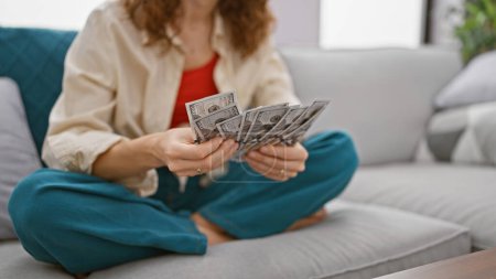 Photo for American woman's hands counting dollar banknotes while sitting on a sofa at home, economy, investment and savings in the united states - Royalty Free Image