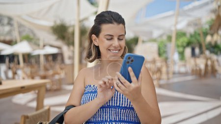 Photo for Young hispanic woman smiling happy using smartphone at sunny restaurant terrace - Royalty Free Image
