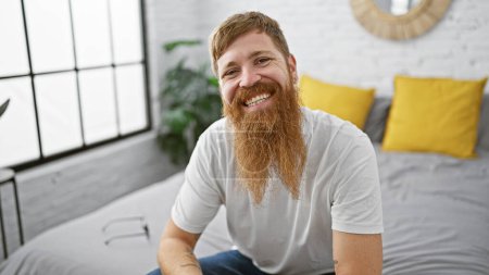 Photo for Wake up to a charming morning with a young, happy redhead man, sitting comfortably in bed, smiling confidently in his cozy bedroom, enjoying a relaxing moment of home comfort. - Royalty Free Image