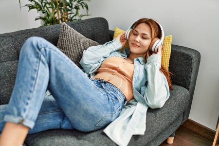 Téléchargez les photos : Young caucasian woman listening to music lying on sofa at home - en image libre de droit