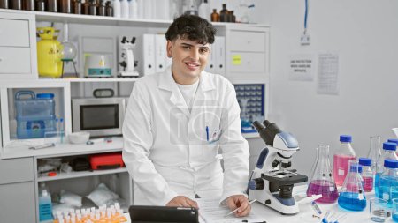 Photo for A young male scientist examines a notebook in a laboratory filled with scientific equipment - Royalty Free Image
