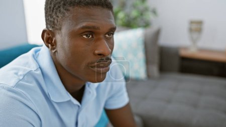 Téléchargez les photos : Bel homme africain adulte posant avec soin dans un cadre de salon moderne. - en image libre de droit