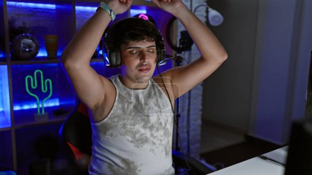 Young man stretching with satisfaction in a neon-lit gaming room, embodying relaxation, entertainment, and modern home leisure.