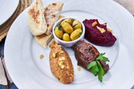 Foto de Un plato de aperitivo mediterráneo con hummus, aceitunas, remolacha, pan de pita y tapenade en un plato blanco. - Imagen libre de derechos