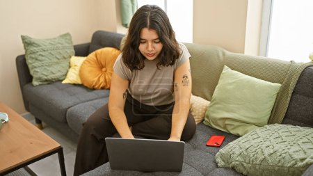 Foto de Una joven hispana trabajando en un portátil en su acogedor apartamento - Imagen libre de derechos