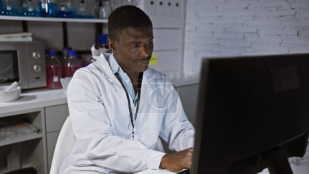 Afrikaner im Laborkittel arbeitet am Computer in einem modernen Laborumfeld