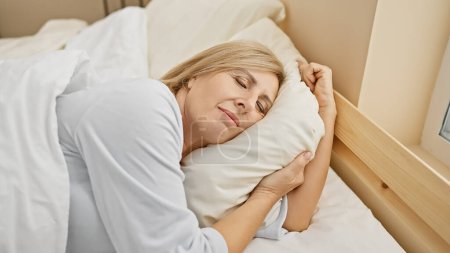 Photo for A peaceful middle-aged blonde woman sleeping comfortably alone in a cozy bedroom setting. - Royalty Free Image