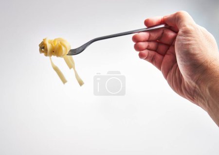 Foto de Una mano sostiene un tenedor girado con pasta fettuccine sobre un fondo blanco - Imagen libre de derechos