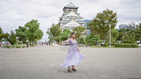 Hermosa mujer hispana girando alegremente en un vestido impresionante alrededor del antiguo castillo osaka - un punto culminante de vacaciones alegres en medio de la herencia japonesa