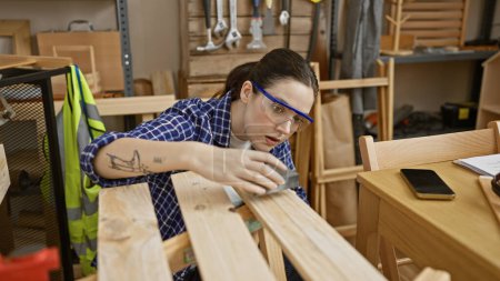 Téléchargez les photos : Une femme concentrée ponçant des meubles en bois dans un atelier de menuiserie bien équipé - en image libre de droit