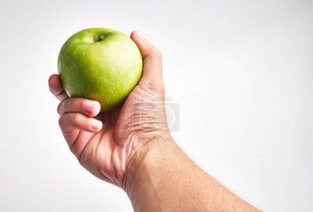Photo for Close-up of a man holding a fresh, green apple against a bright white background - Royalty Free Image