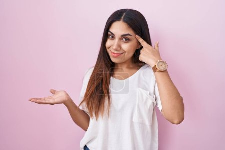 Photo for Young arab woman standing over pink background confused and annoyed with open palm showing copy space and pointing finger to forehead. think about it. - Royalty Free Image