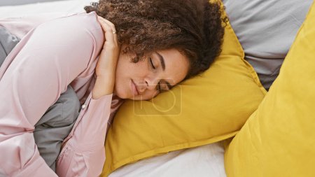 Photo for A beautiful young hispanic woman with curly hair peacefully sleeping in a bedroom with yellow pillows - Royalty Free Image