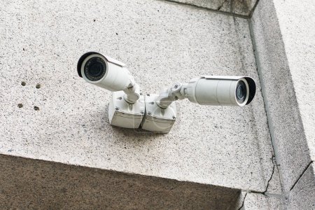 Téléchargez les photos : Deux caméras de surveillance blanches attachées à un coin de bâtiment en béton gris pour la surveillance de la sécurité. - en image libre de droit