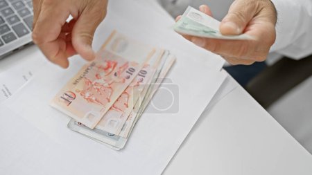 Photo for Middle-aged man handing out singaporean currency in a well-lit office environment, suggesting a financial transaction or business activity. - Royalty Free Image