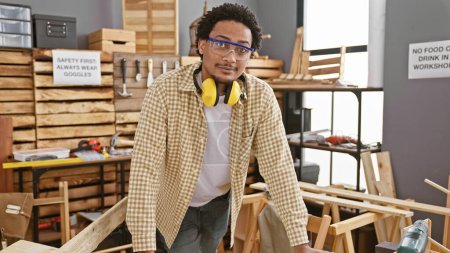 Handsome young man with curly hair wearing safety glasses and ear protection in a carpentry workshop.