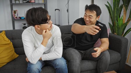 Photo for Two asian men relaxing and watching television together in a cozy living room setting - Royalty Free Image