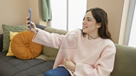Photo for A young woman takes a selfie in a cozy living room, lighting up the space with her radiant smile. - Royalty Free Image