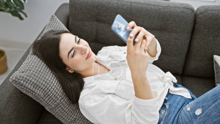 Femme détendue naviguant smartphone sur le canapé dans un cadre confortable salon