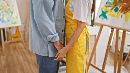 Téléchargez les photos : Couple d'artistes tenant la main dans un studio lumineux avec des peintures colorées et des chevalets autour. - en image libre de droit