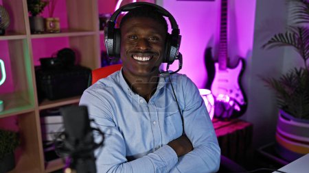 Foto de Un hombre afroamericano alegre usando auriculares en una colorida sala de juegos por la noche. - Imagen libre de derechos