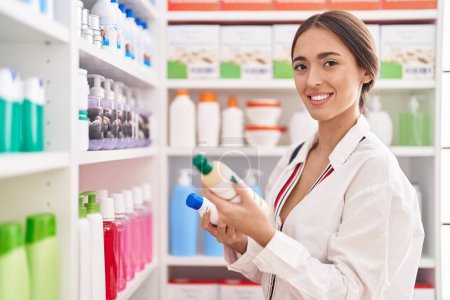 Téléchargez les photos : Jeune belle hispanique femme client souriant confiant tenant bouteilles de shampooing à la pharmacie - en image libre de droit