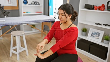 A young hispanic woman stretches her fingers in the interior of a well-equipped rehabilitation clinic.