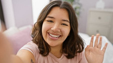 Photo for A cheerful young hispanic woman takes a selfie in a cozy bedroom, radiating warmth and positivity. - Royalty Free Image
