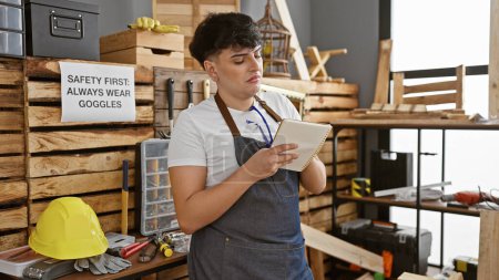 Photo for A young man takes notes in a well-organized carpentry workshop filled with tools and safety equipment. - Royalty Free Image