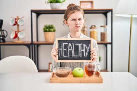 Photo for Frowning young blonde woman facing problems, skeptical and nervous while enjoying healthy breakfast at home, clearly upset. - Royalty Free Image