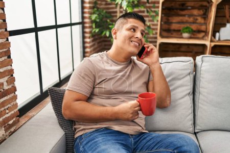 Téléchargez les photos : Jeune homme latino parlant sur smartphone boire du café à la maison - en image libre de droit