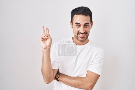 Photo for Handsome hispanic man standing over white background smiling with happy face winking at the camera doing victory sign with fingers. number two. - Royalty Free Image