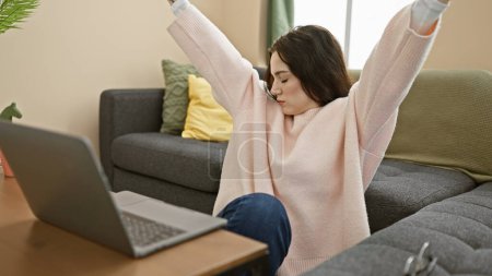Téléchargez les photos : Une jeune femme détendue s'étire tout en prenant une pause de son ordinateur portable dans un salon confortable. - en image libre de droit